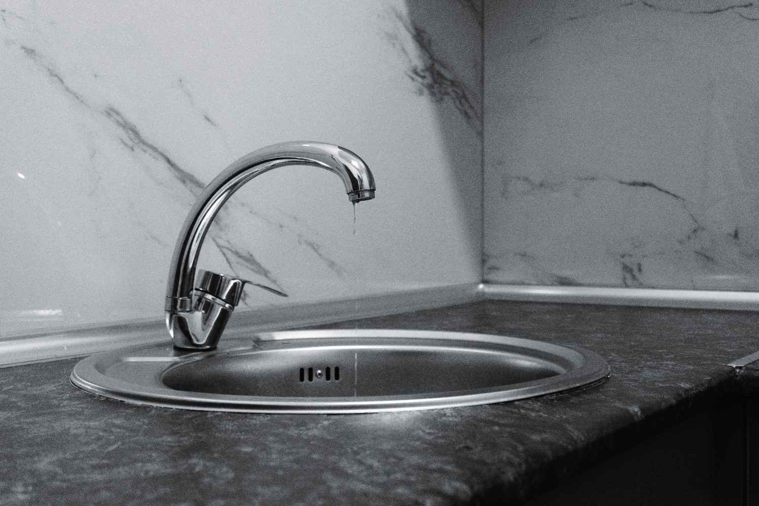 A clean and modern kitchen sink with a dripping chrome faucet