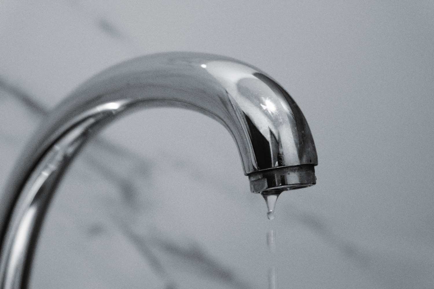 A close-up shot of a modern chrome bathroom faucet with water dripping from the tip