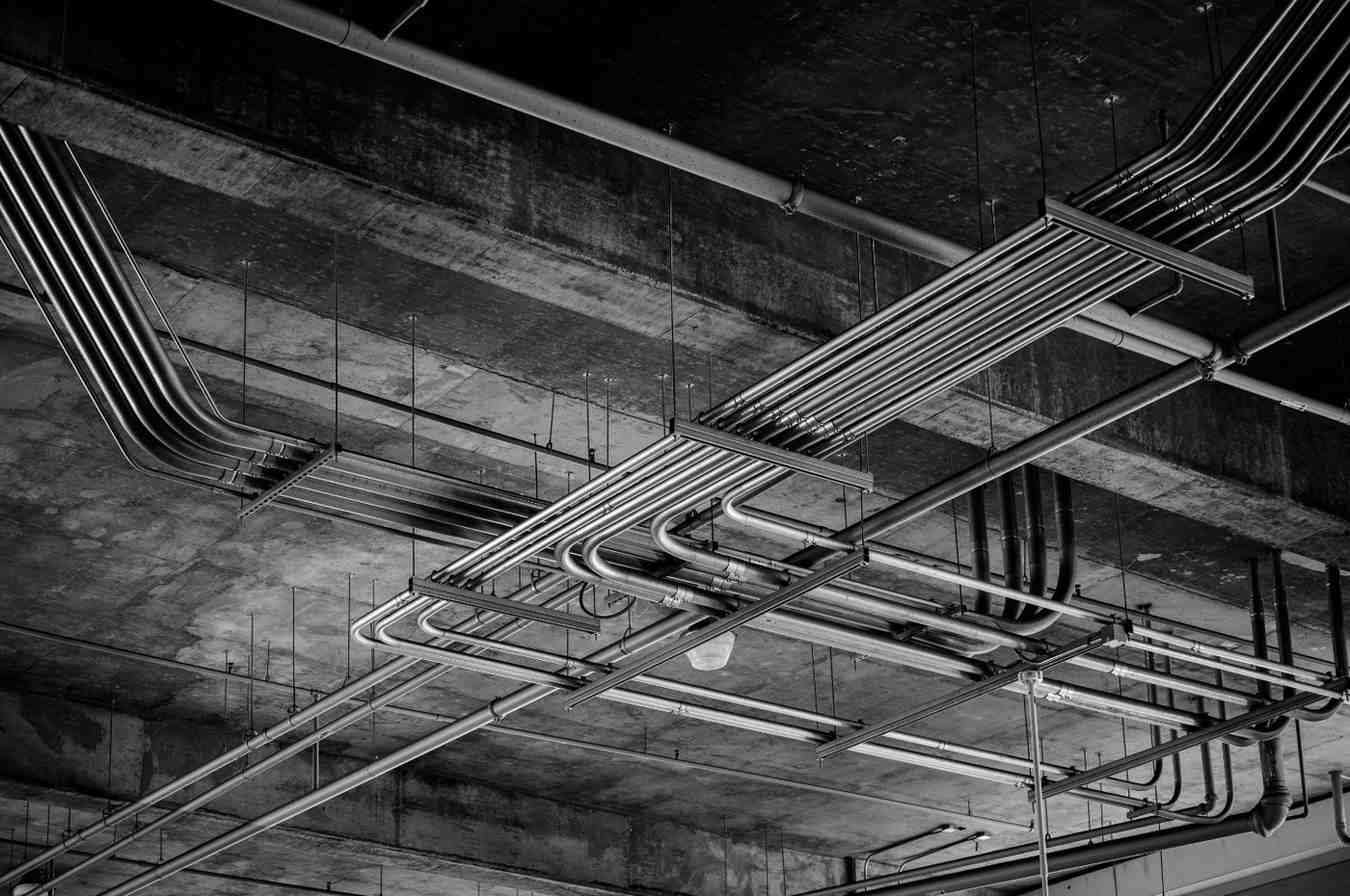 Black and white photo of industrial ceiling with metal pipelines