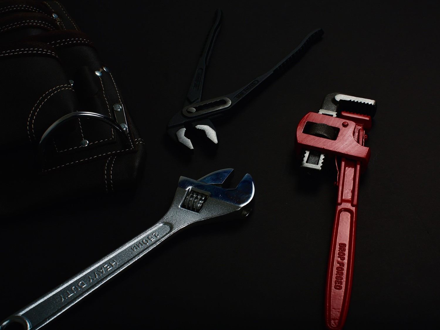 Close-up of various hand tools including wrenches and pliers on a dark surface